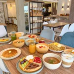 Mesa completa del desayuno buffet de Artesano en Ibarra con waffles, pancakes, jugos, cereales, frutas y platos típicos ecuatorianos en un ambiente moderno.